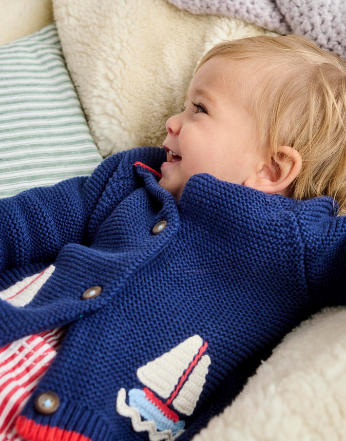 Baby laying down wearing Boden knit cardigan.