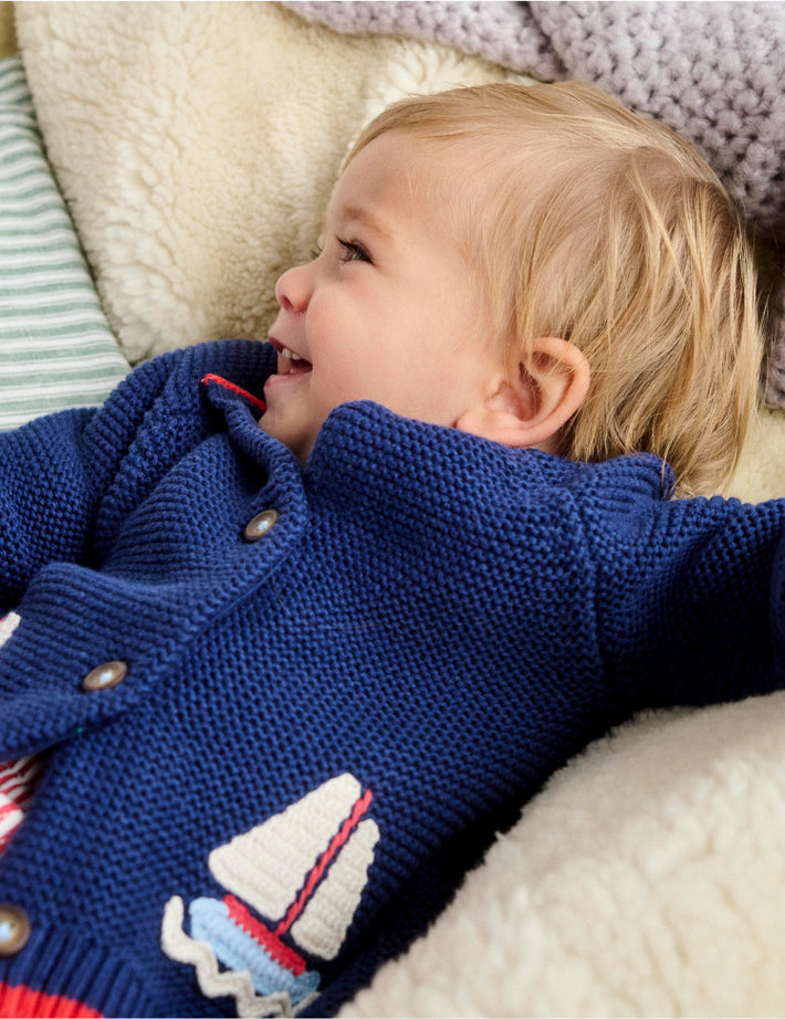 Baby laying down wearing Boden knit cardigan.