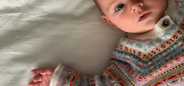 Baby wearing a colorful knitted sweater lying on a white surface