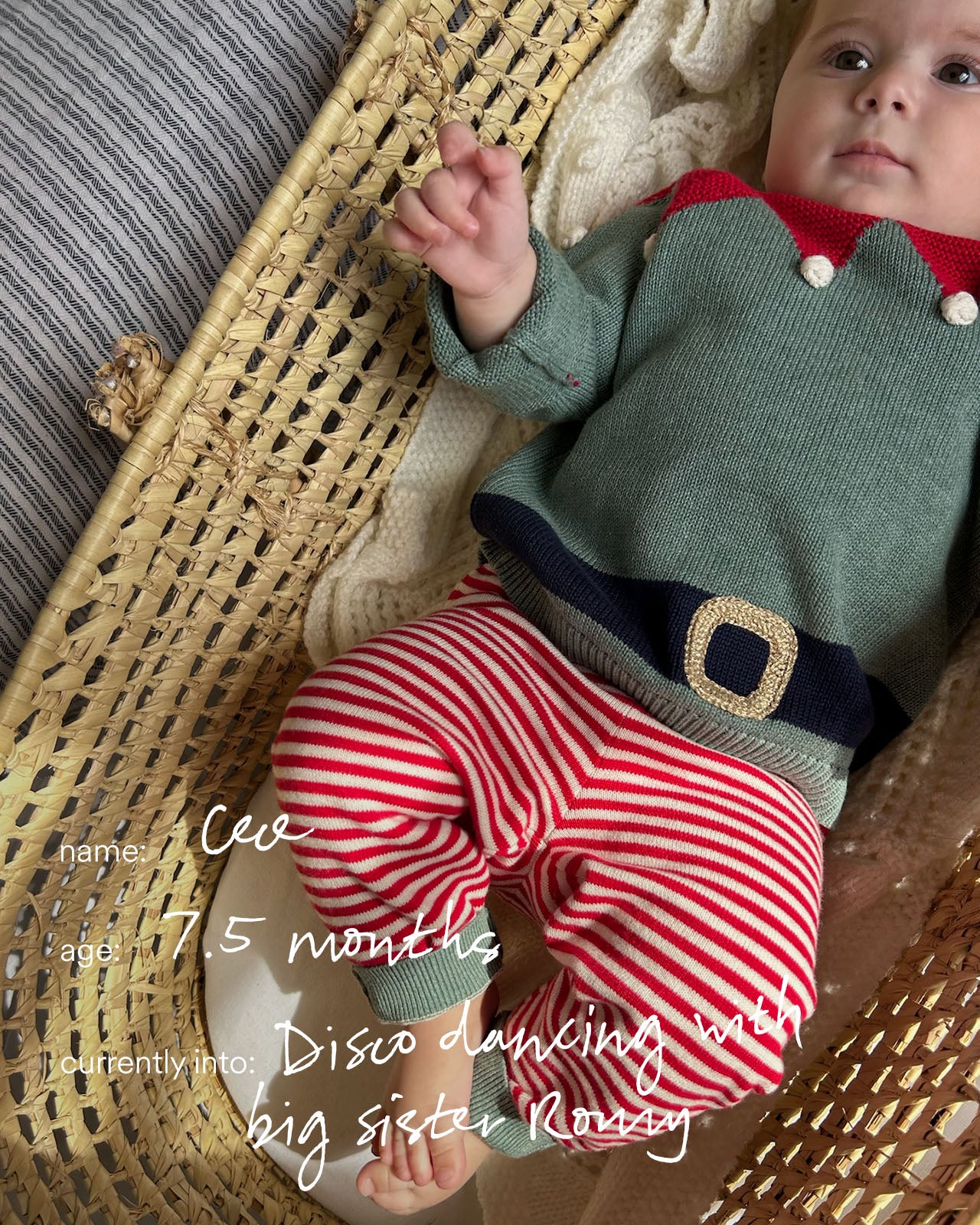 Baby in a green sweater and red striped pants sitting on a textured surface.