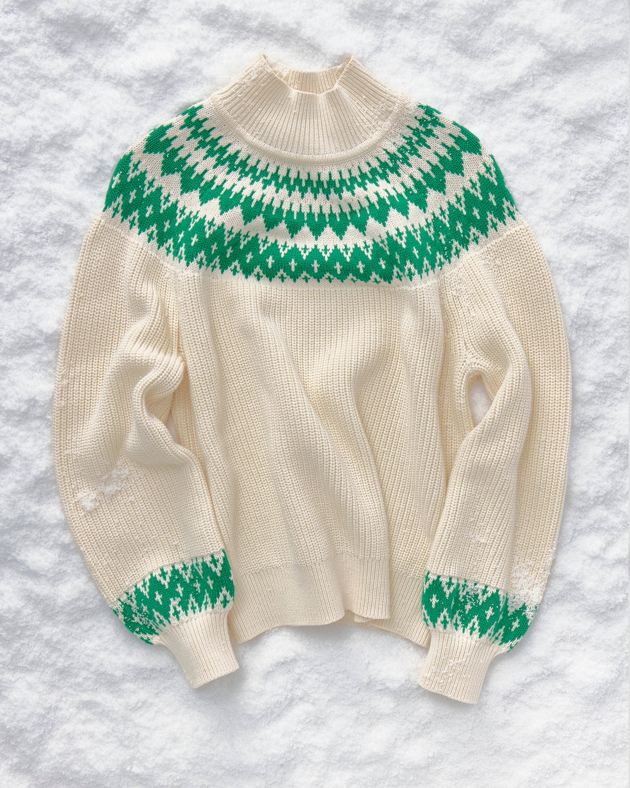 Cream-colored sweater with green pattern on a snowy background