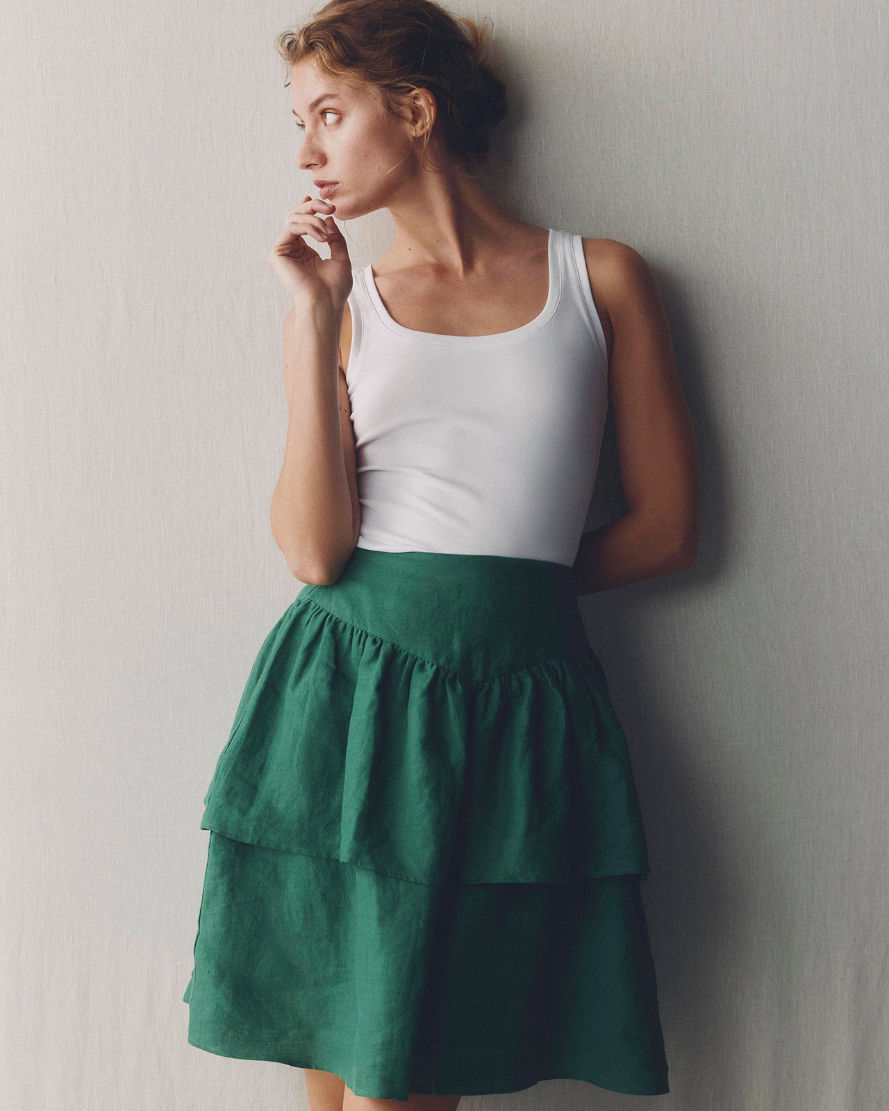 Woman wearing a white tank top and green tiered skirt against a plain background