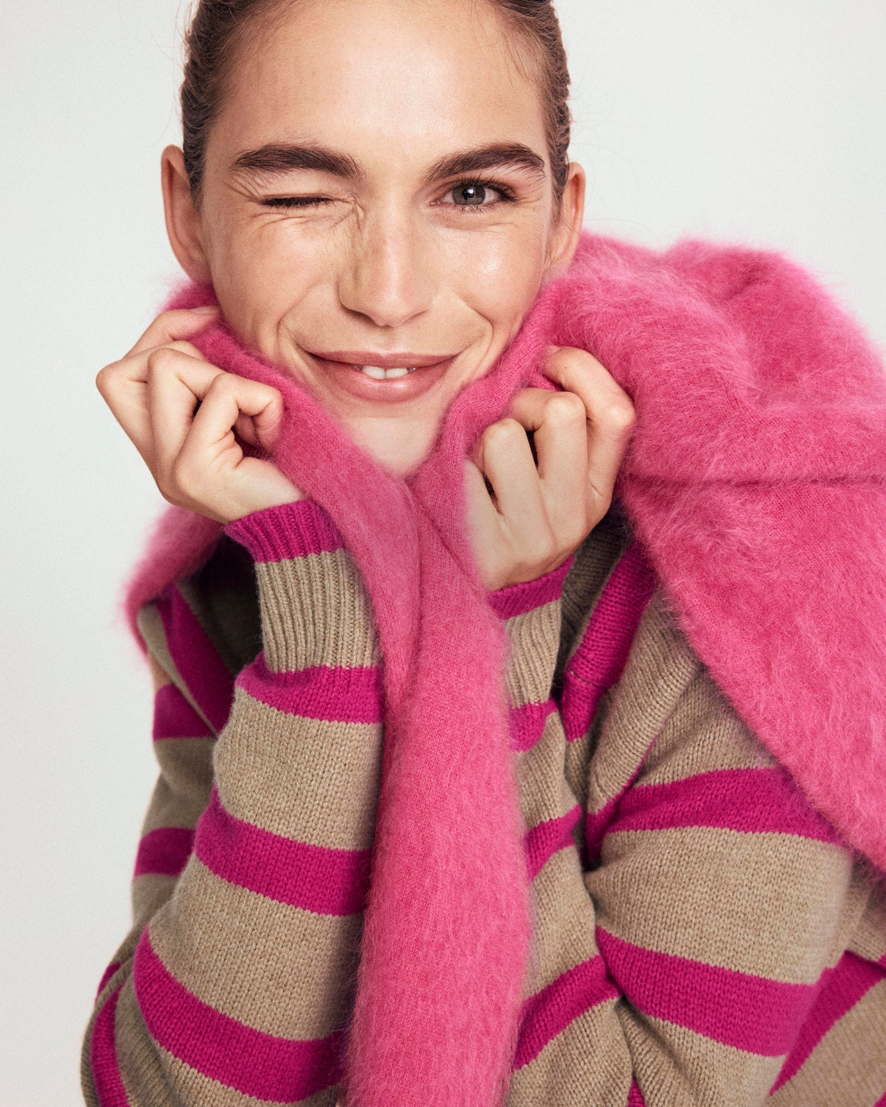 Person wearing a pink and brown striped sweater with a pink fur collar against a white background