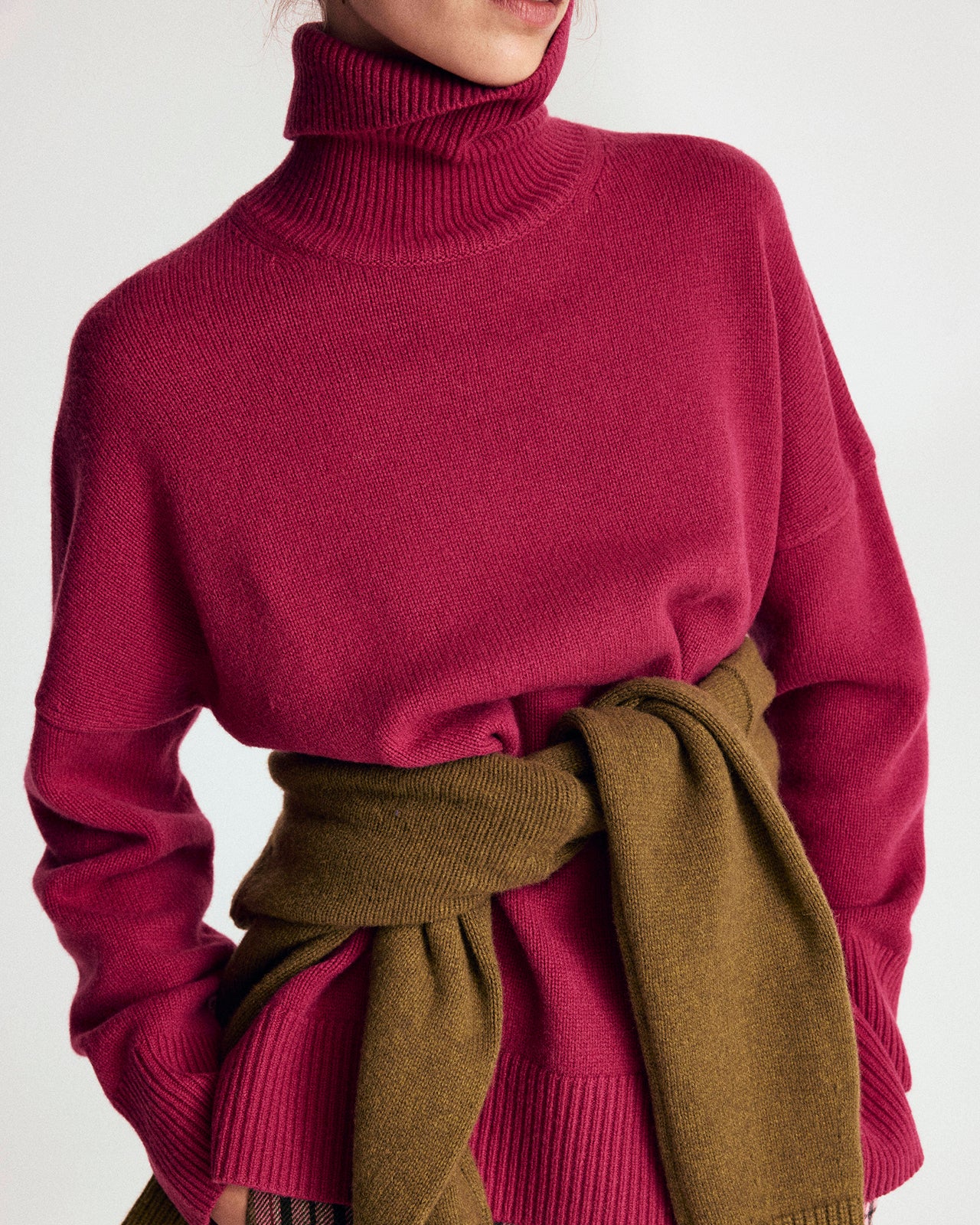 Person wearing a pink turtleneck sweater with a brown scarf on a white background