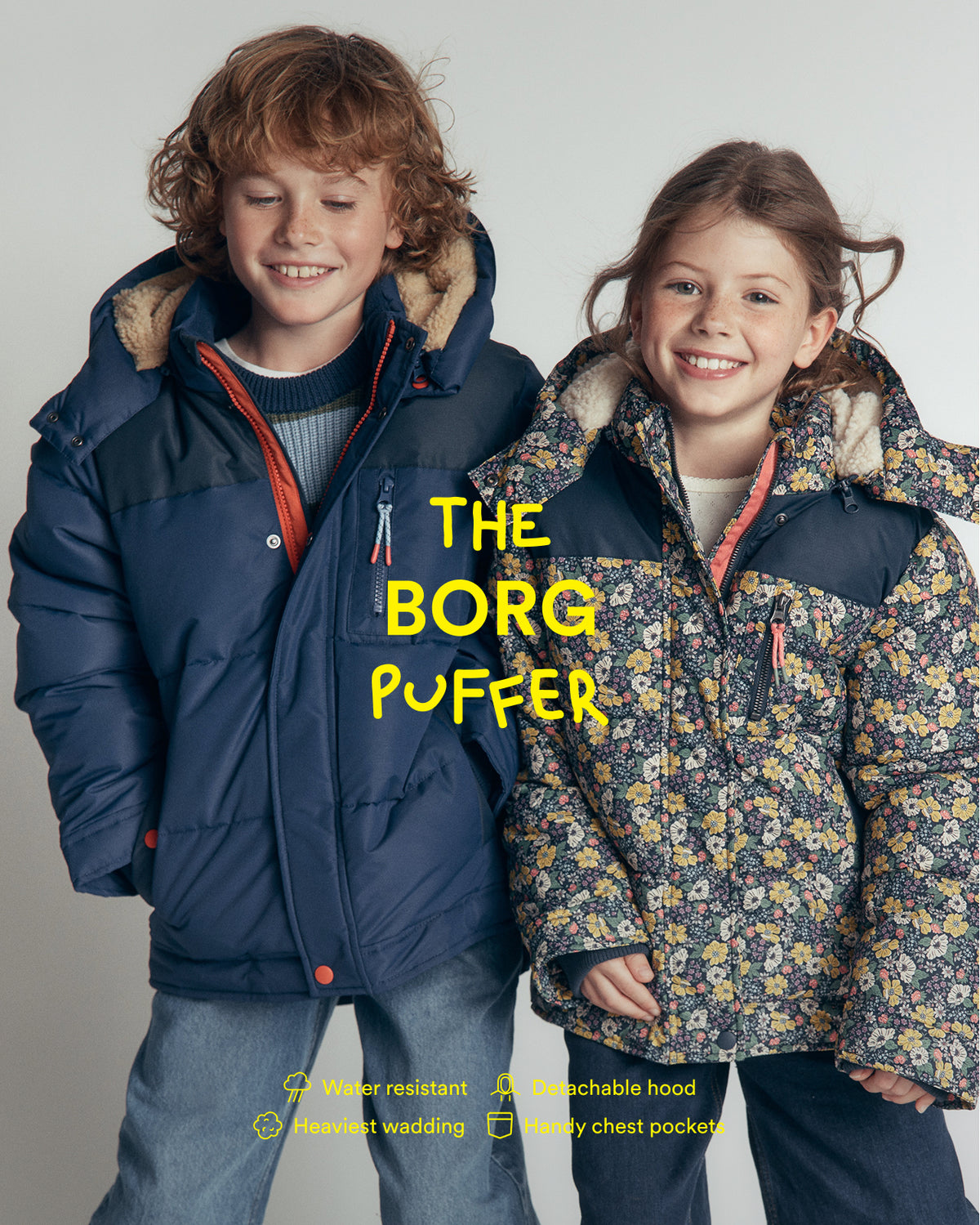 Two children wearing puffer jackets from The Borg Puffer, standing against a light gray studio background. The boy on the left wears a solid navy blue jacket with a tan fleece-lined hood and orange zipper trim.