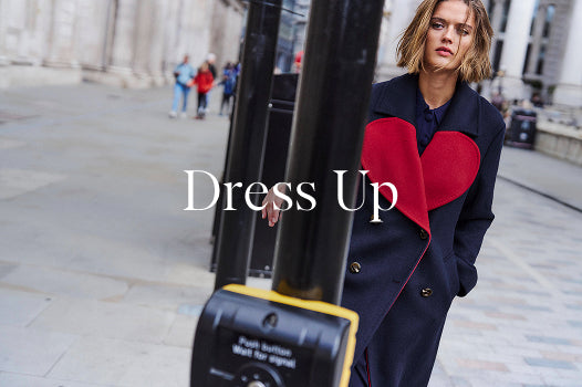 Woman wearing a coat with a red heart design on a city street, with 'Dress Up' text overlay.