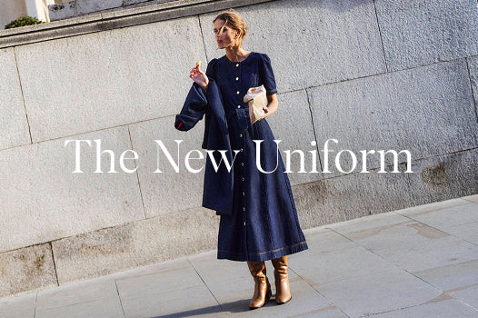 Woman in a long dark blue dress standing against a stone wall with 'The New Uniform' text.