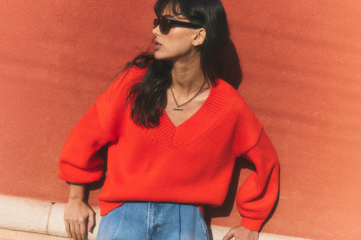 Person wearing a bright red sweater and sunglasses against a red wall.