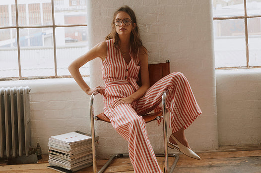 Woman in a red and white striped jumpsuit sitting on a chair in a room with large windows.