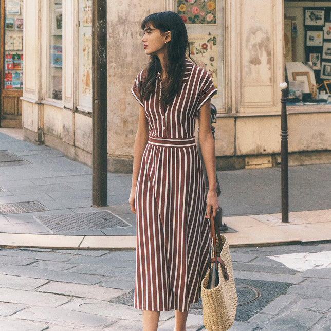Woman in a striped dress standing on a street with a store in the background