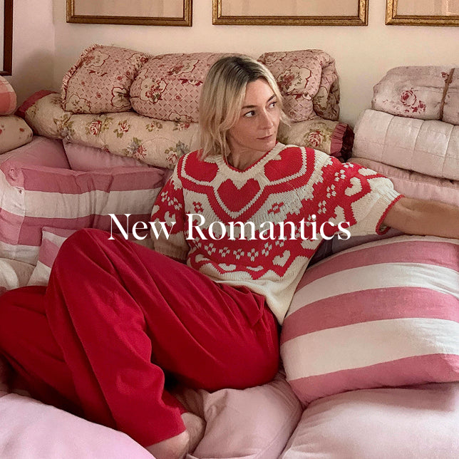 Woman sitting on a floral-patterned couch wearing a red and white sweater with heart designs.