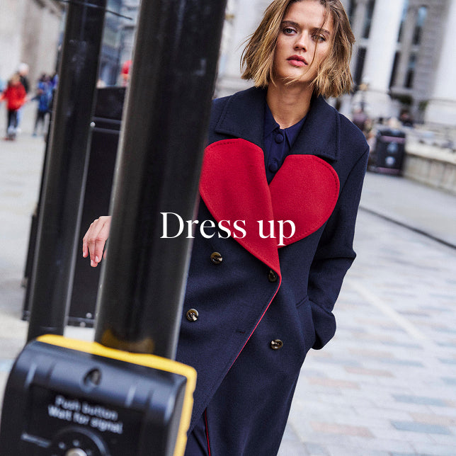 Woman wearing a coat with a red heart design on a city street, with text 'Dress up'.