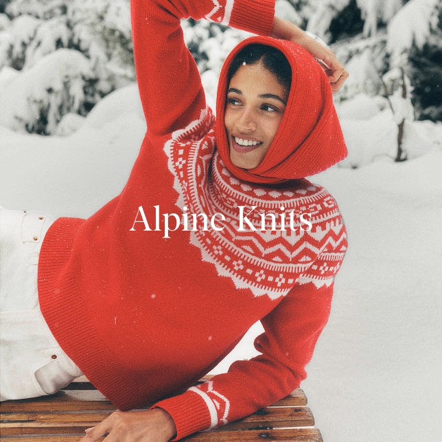 Person wearing a red knitted outfit with white patterns, lying on a snowboard in a snowy landscape. 'Alpine Knits' text overlay.