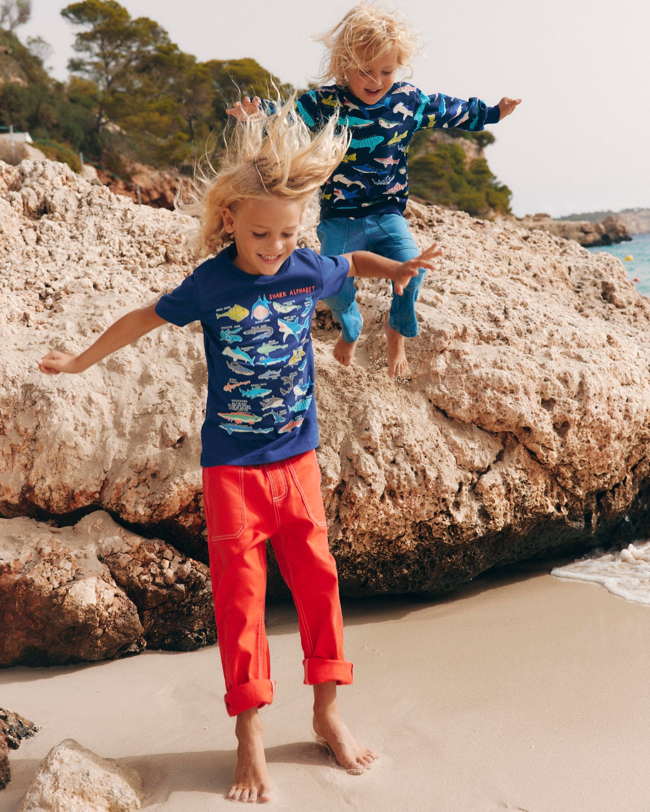 Two boys jumping wearing shark themed t shirts. Image link to Childrens tops & t-shirts.