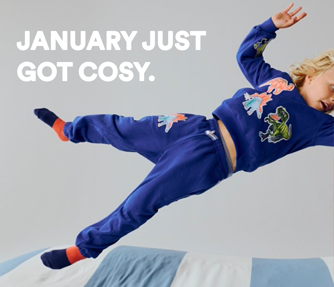 Child in blue pajama set with dinosaur designs on a light gray background, text 'January just got cosy'.