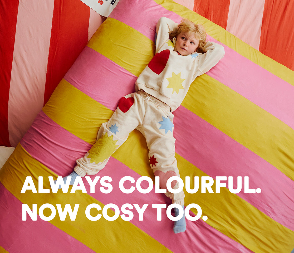 Child lying on a colorful striped bed with text 'Always Colourful. Now Cosy Too.'