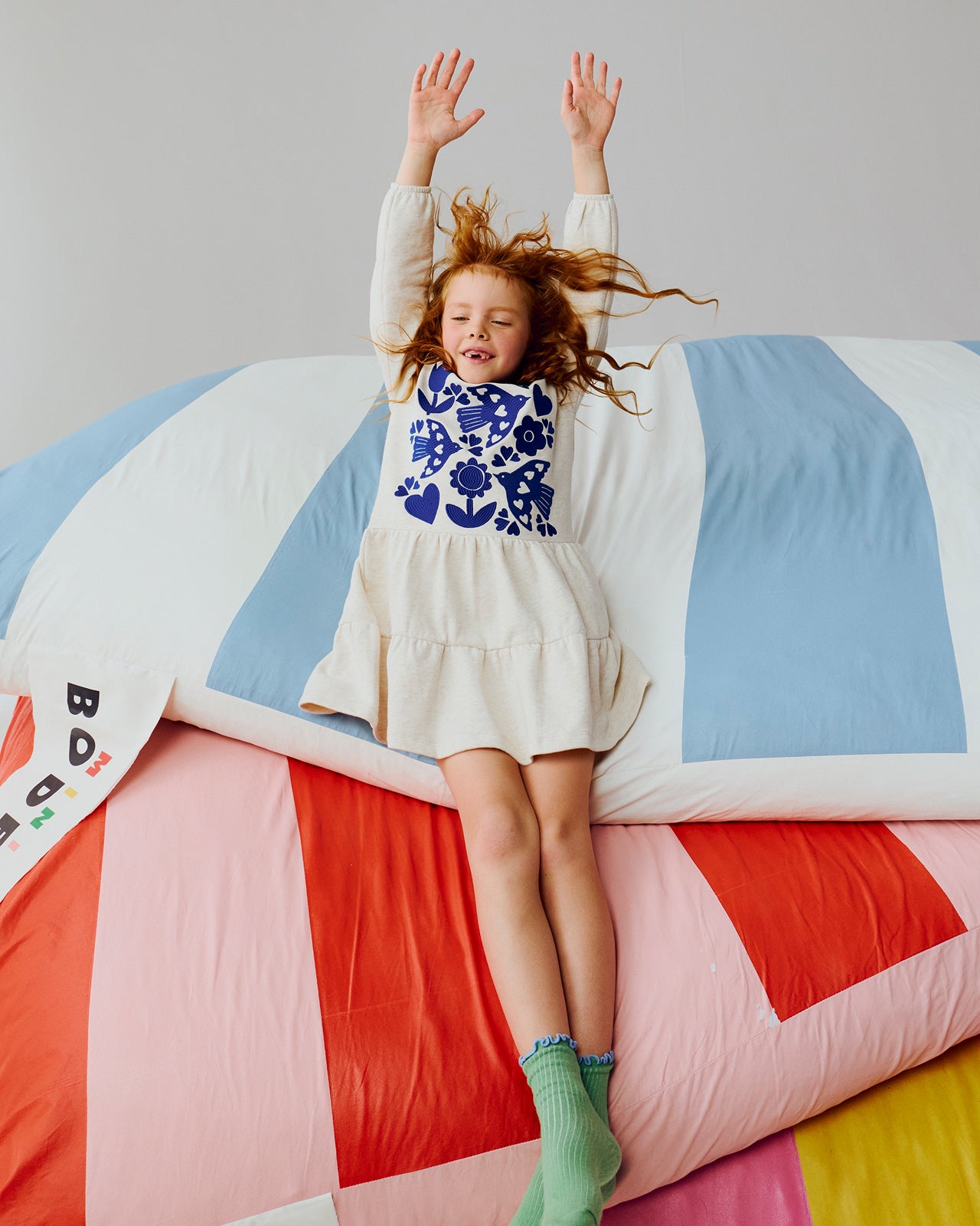 Child in a colorful dress with blue floral pattern on a striped bedspread