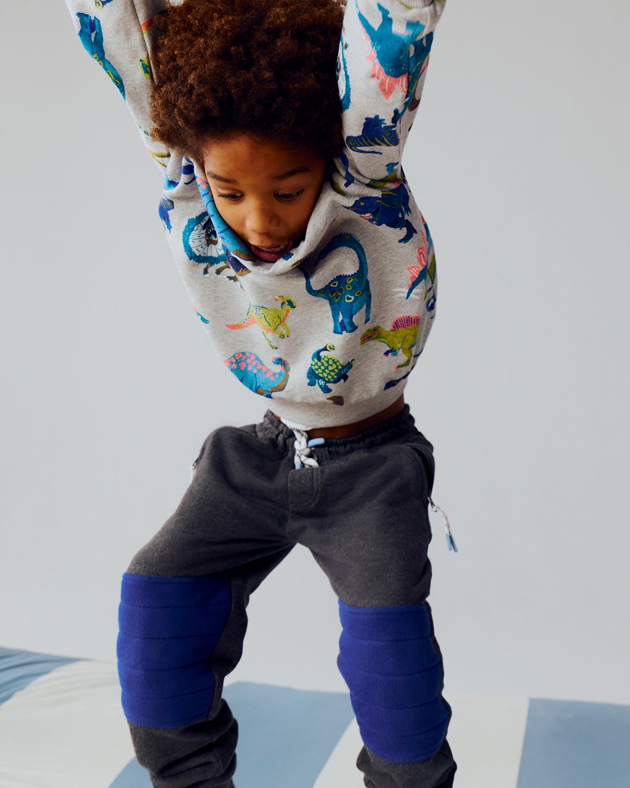 Child wearing a hoodie with dinosaur pattern and gray pants on a light background