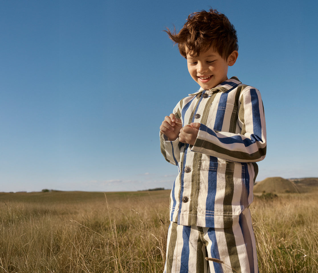 Child in a striped outfit standing in a field with a clear blue sky.