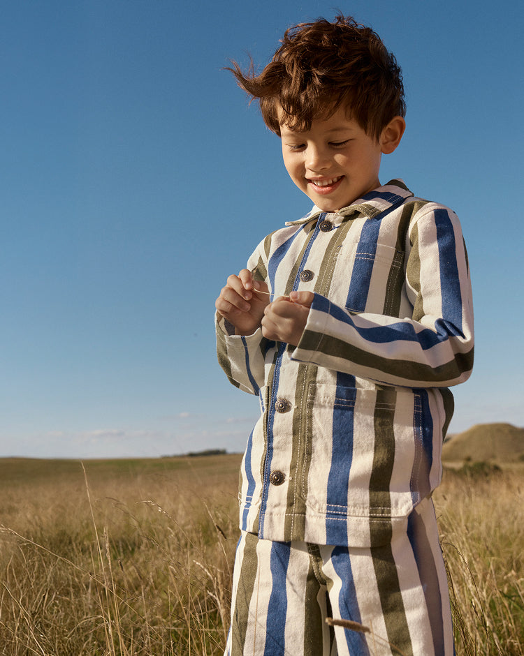 Child in a striped outfit standing in a field with a clear blue sky.