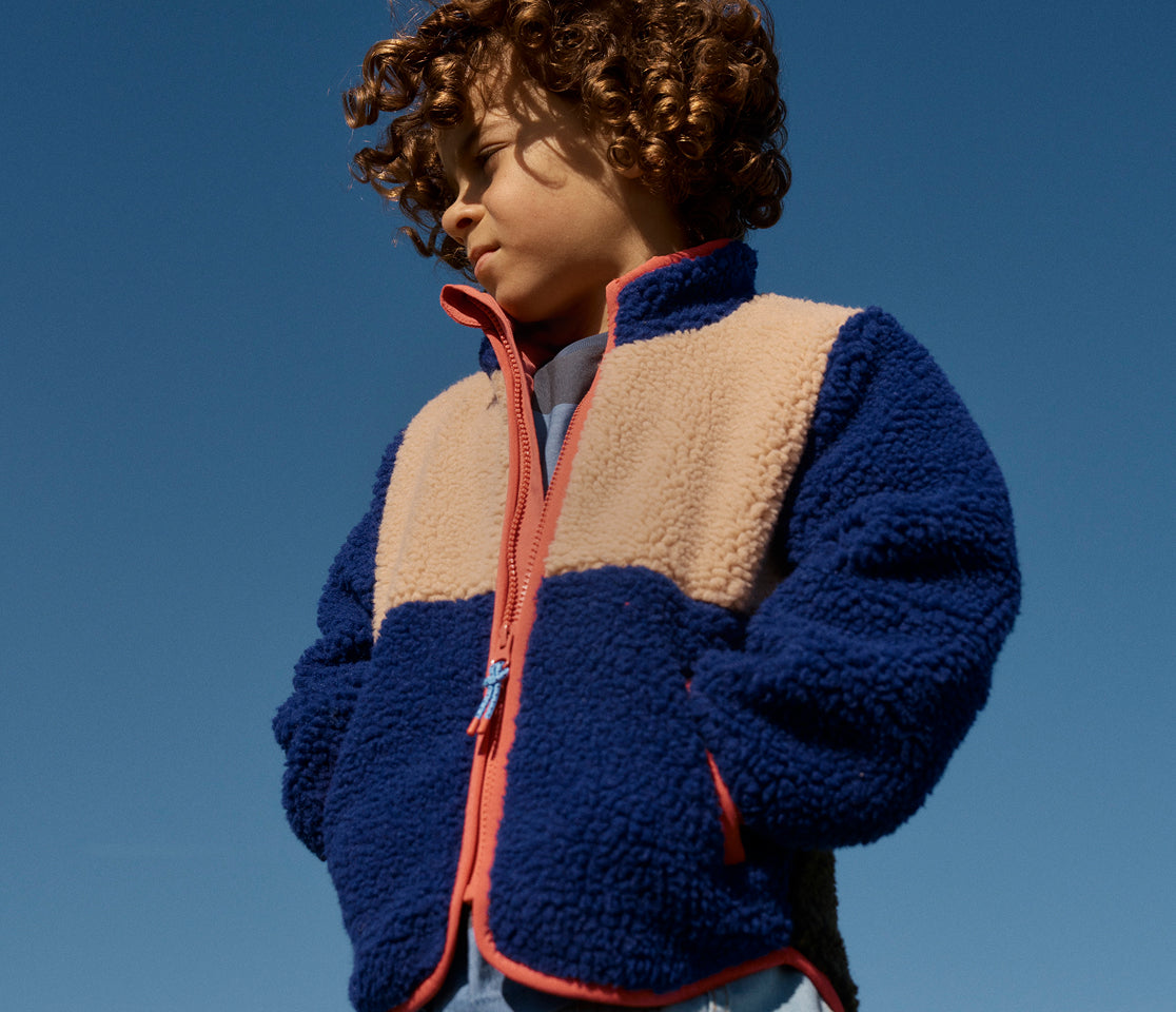 Child wearing a colorful fleece jacket against a clear blue sky