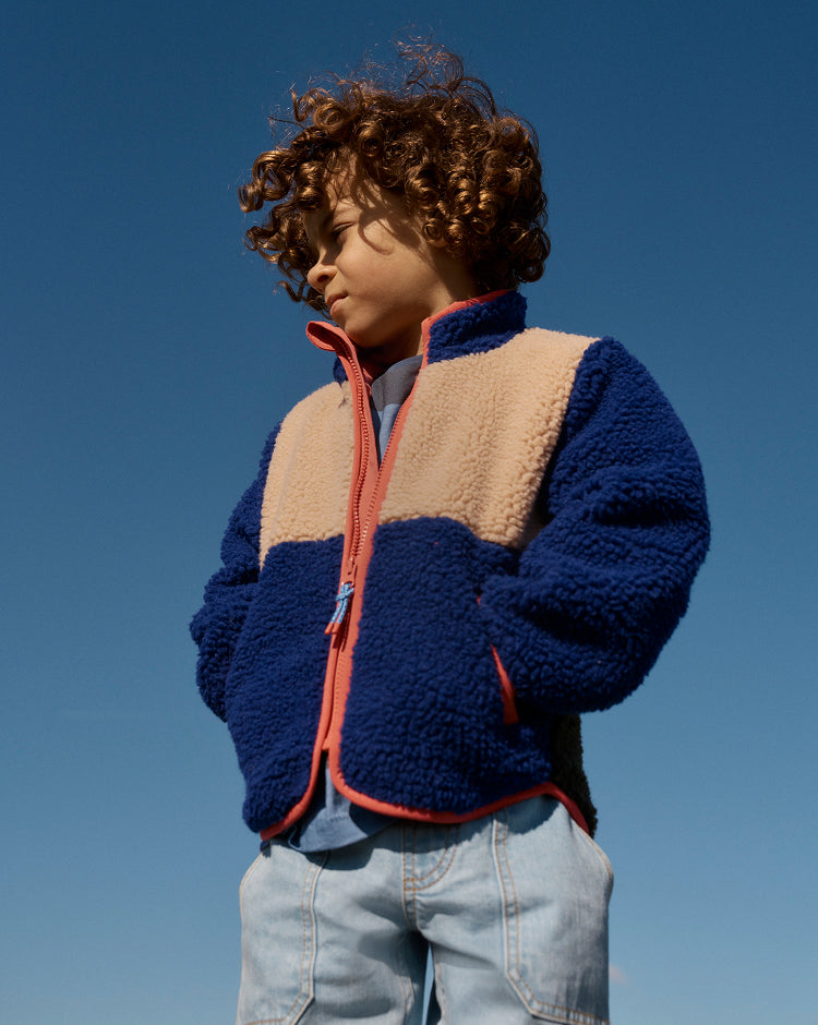 Child wearing a blue and beige fleece jacket against a clear blue sky