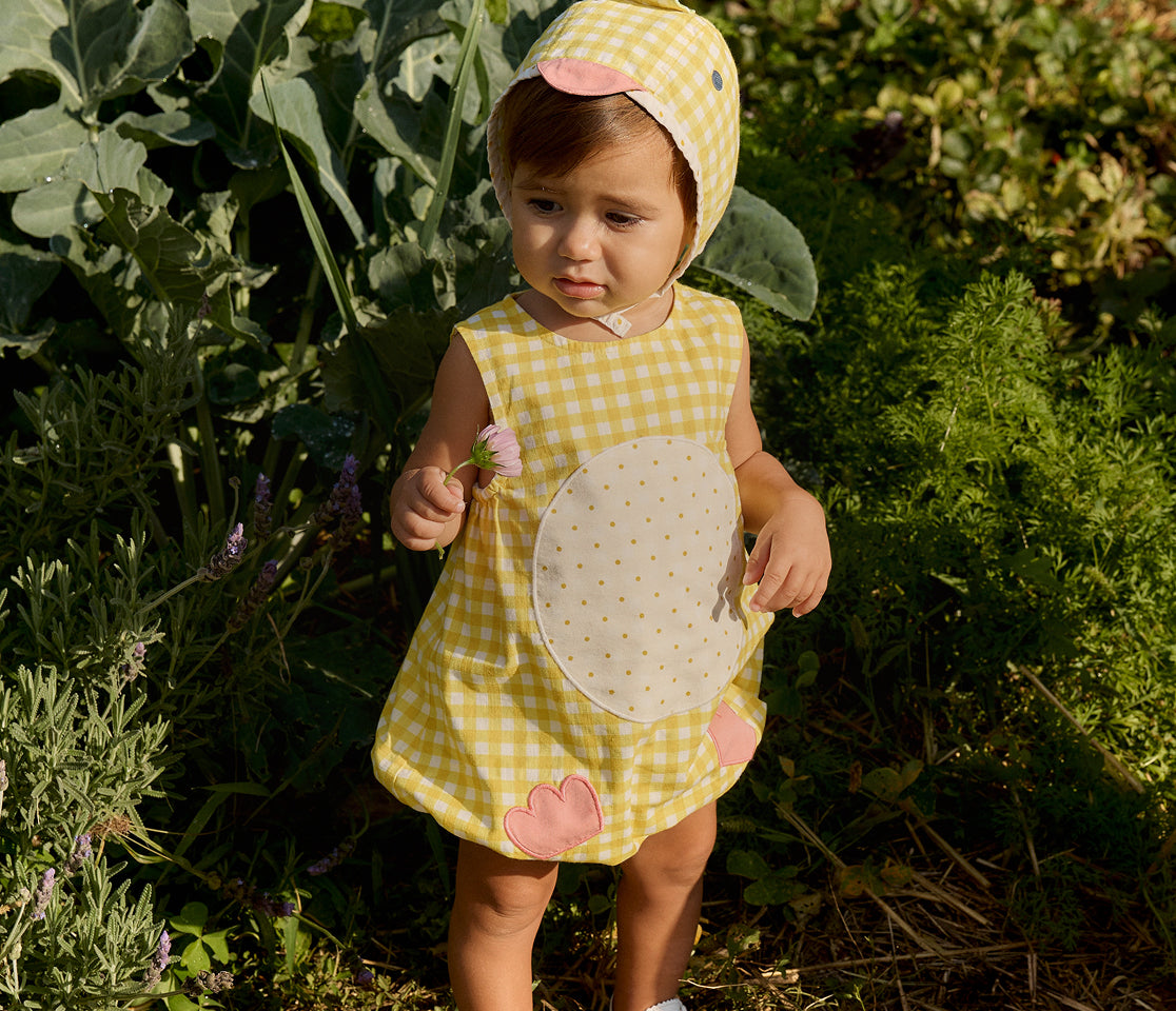 Child in a yellow checkered dress with bunny ears standing in a garden.