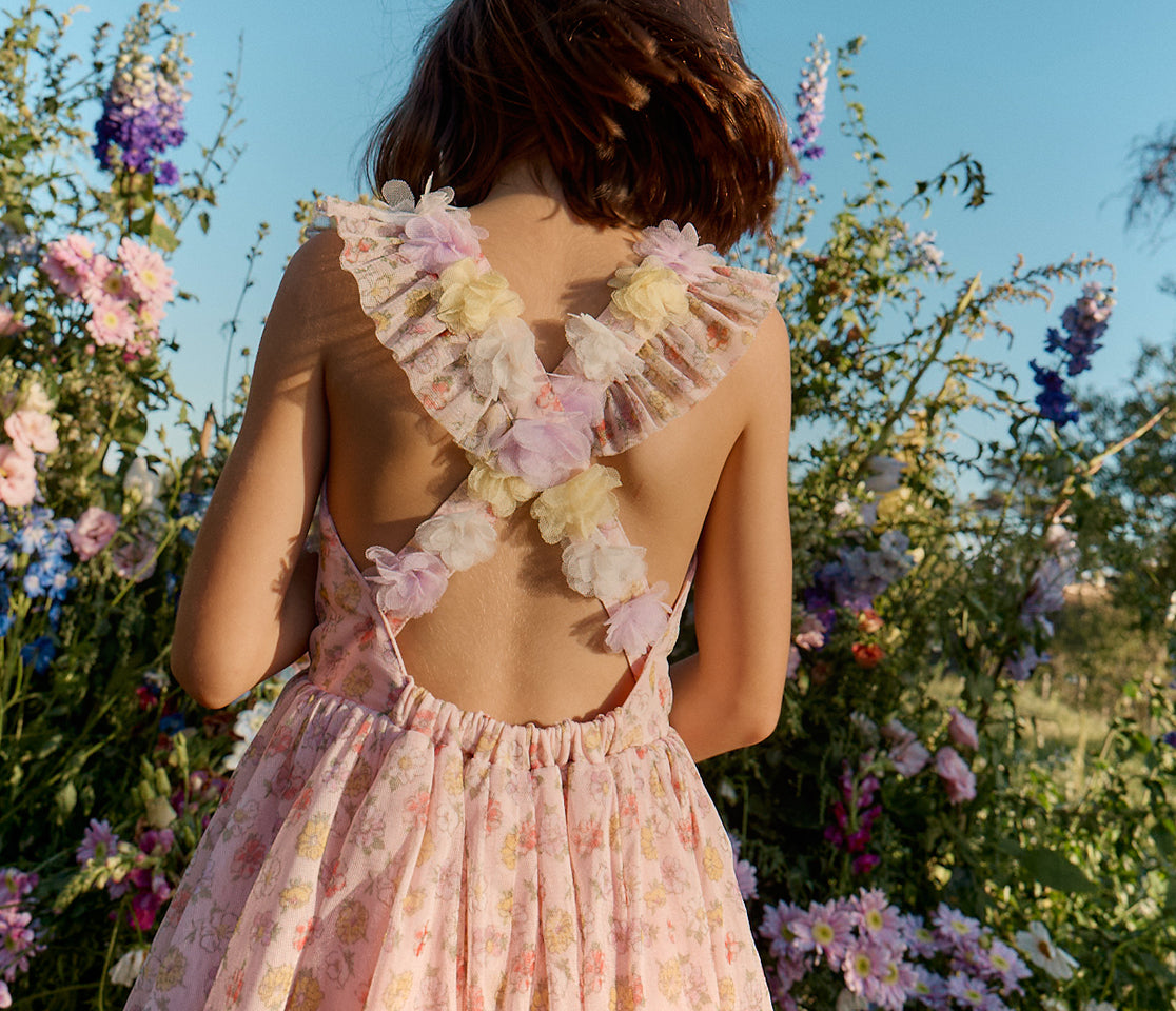 Girl in a floral dress standing in a field of flowers with a clear blue sky.