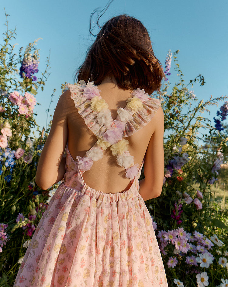 Girl in a floral dress standing in a field of flowers with a clear blue sky.