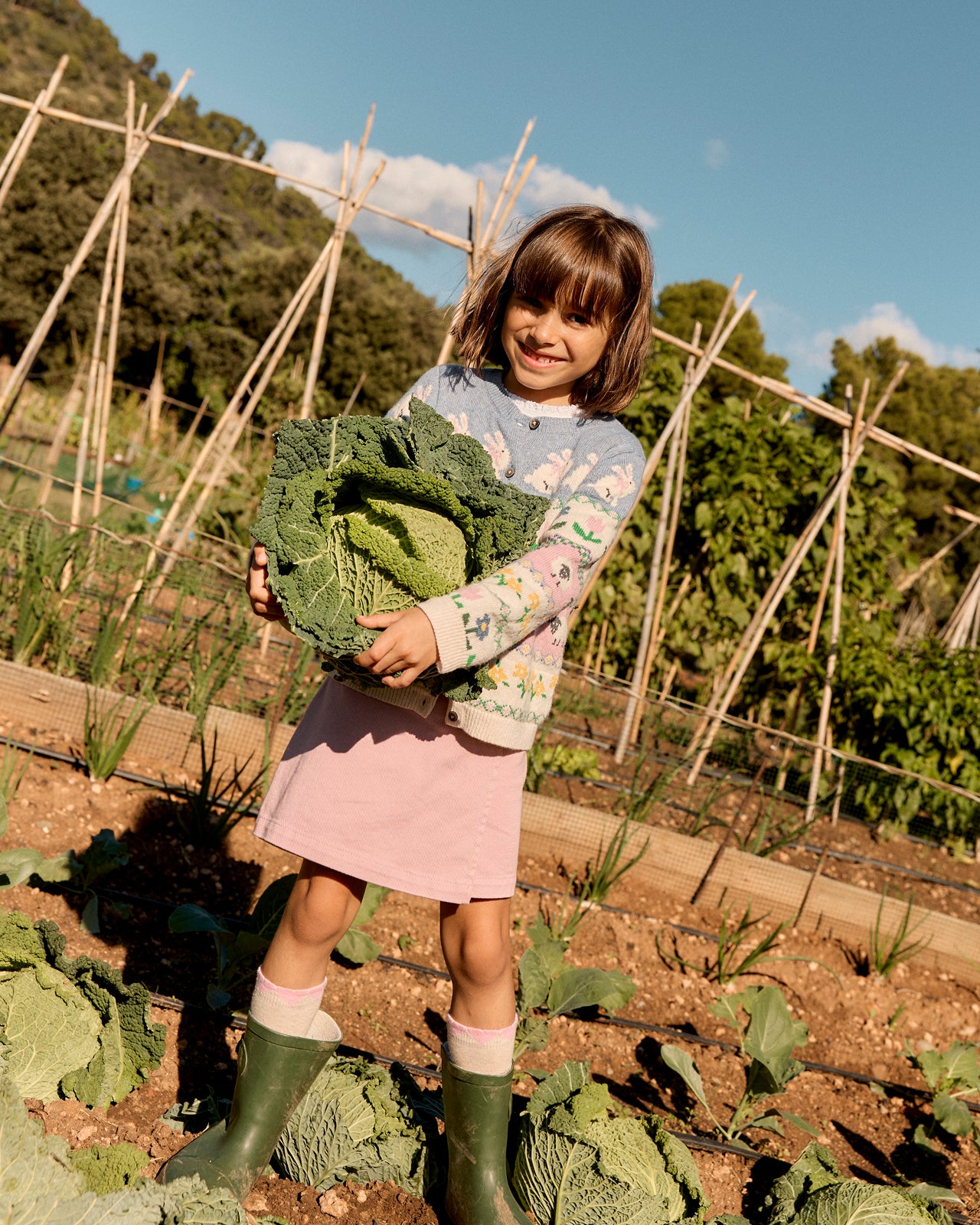 Young girl holding a large green cabbage in a garden