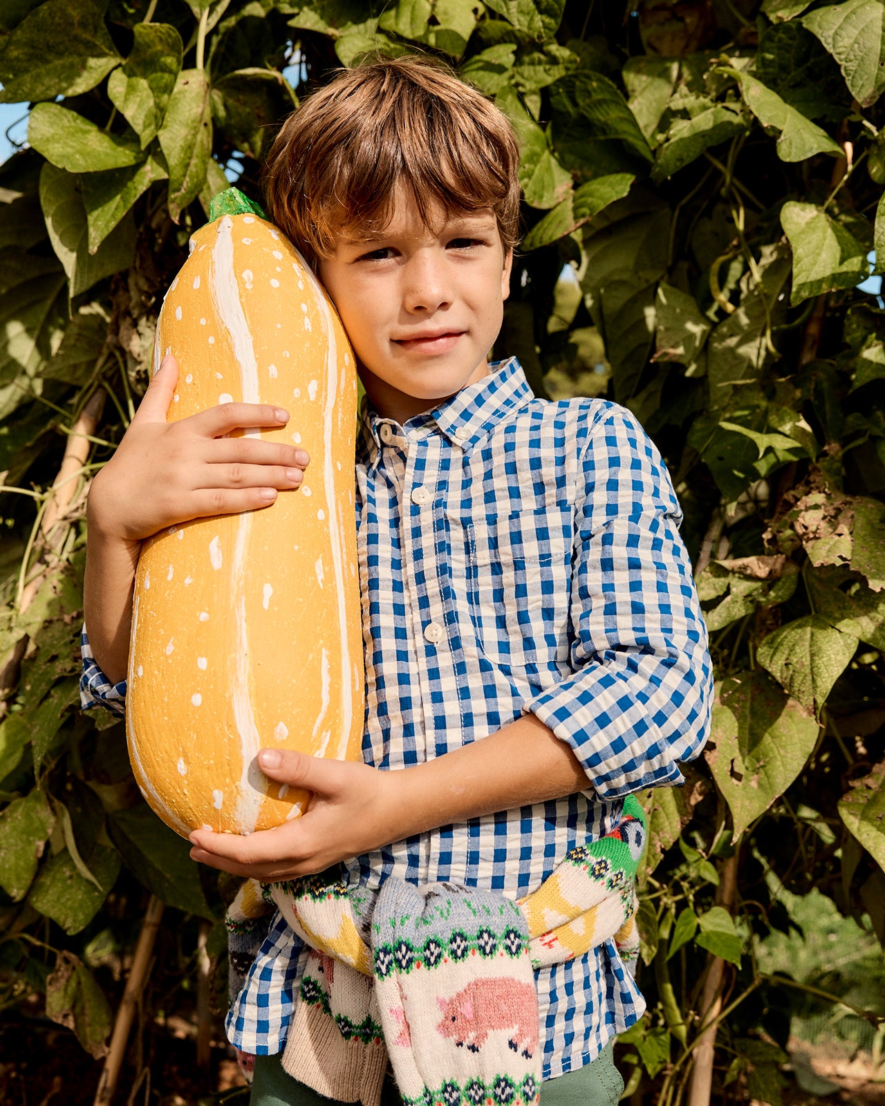 Child holding a large yellow pumpkin with white spots in a garden setting