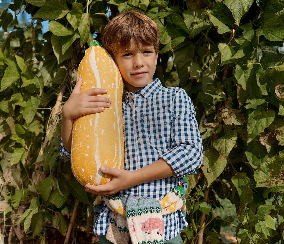 Child holding a large pumpkin outdoors among green leaves