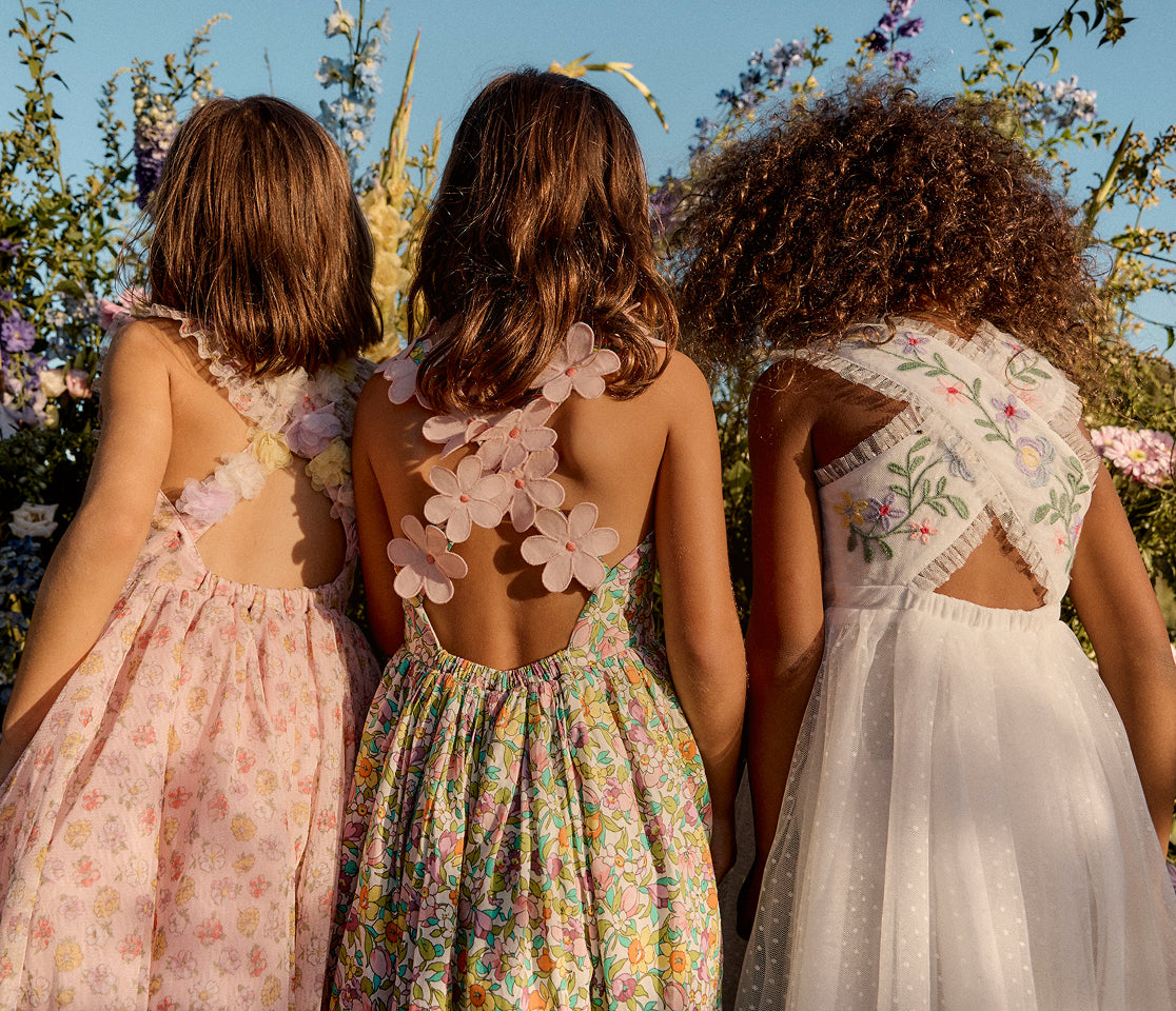 Three girls wearing floral dresses standing in a field of flowers.