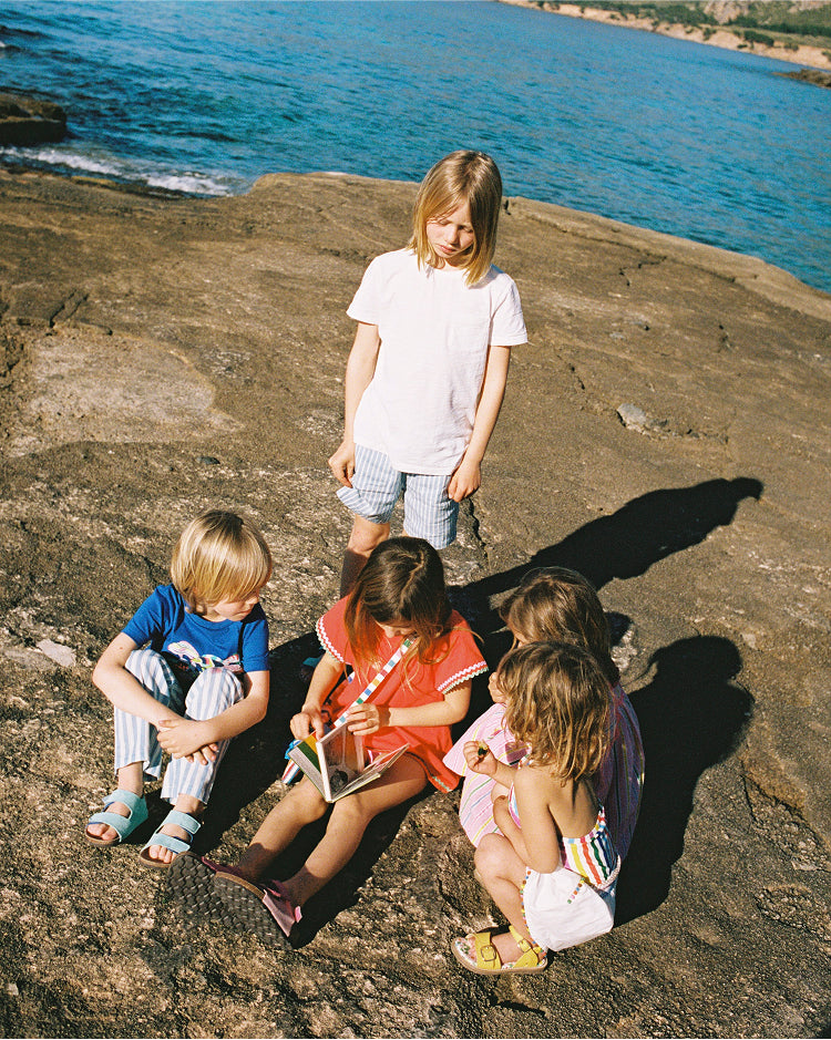 Kids sat by the sea wearing colourful Boden holiday clothes