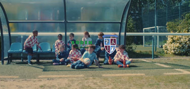 Children playing soccer on a grassy field with a school emblem in the background