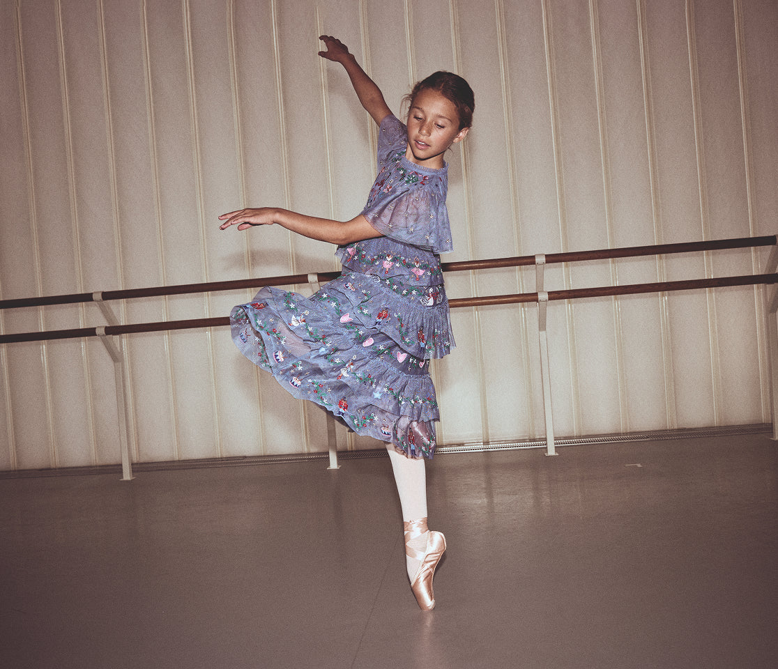 Young dancer in a floral dress practicing ballet in a studio.