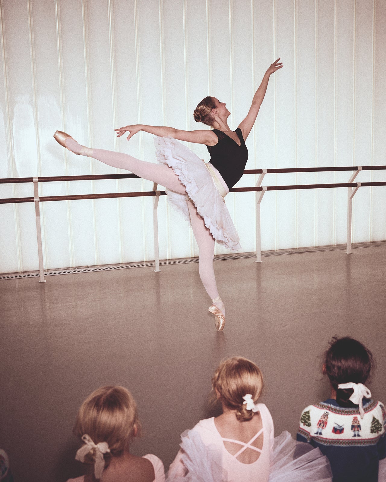 Ballerina practicing in a ballet studio with onlookers.