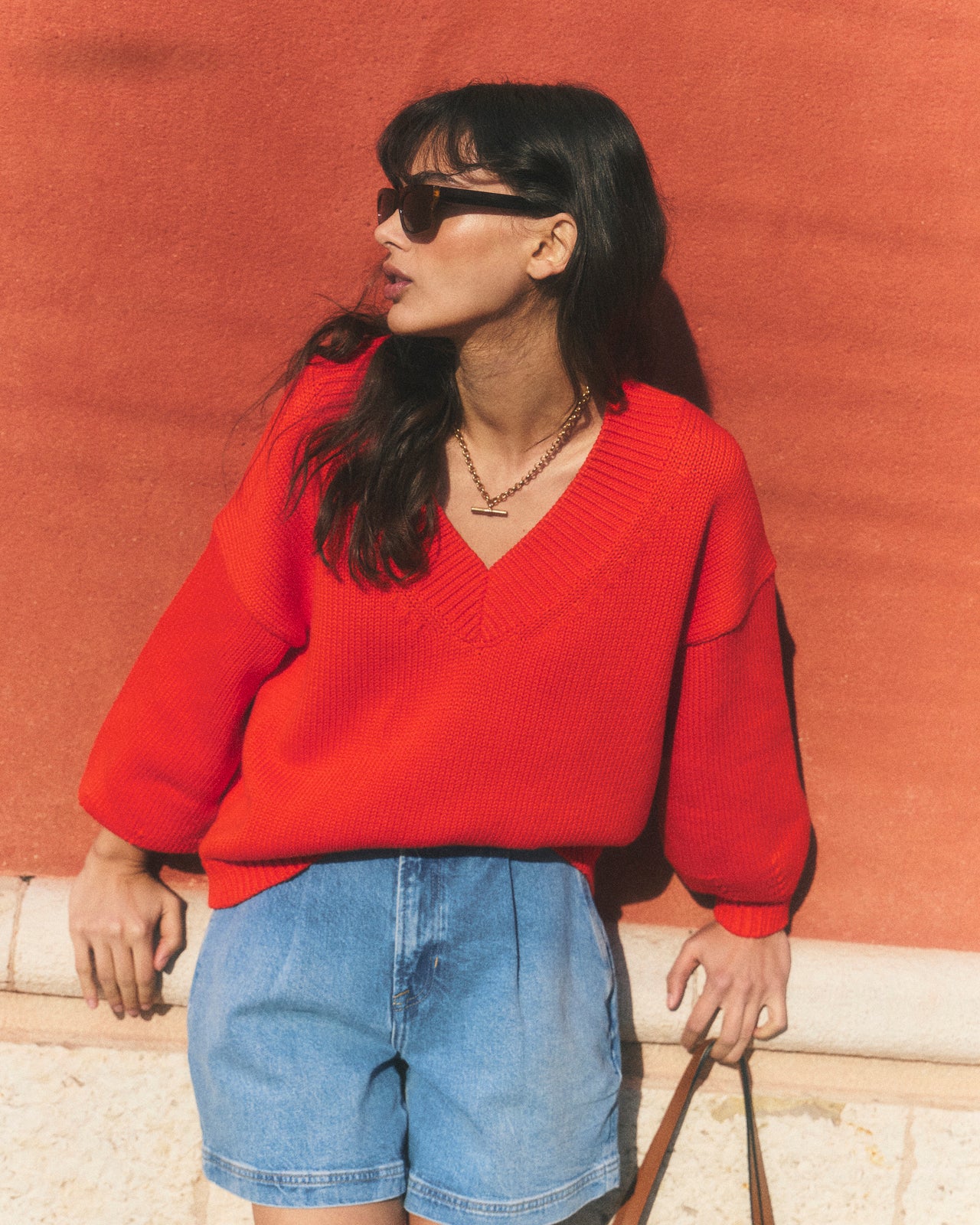 Woman wearing a red sweater and blue shorts against a red wall.