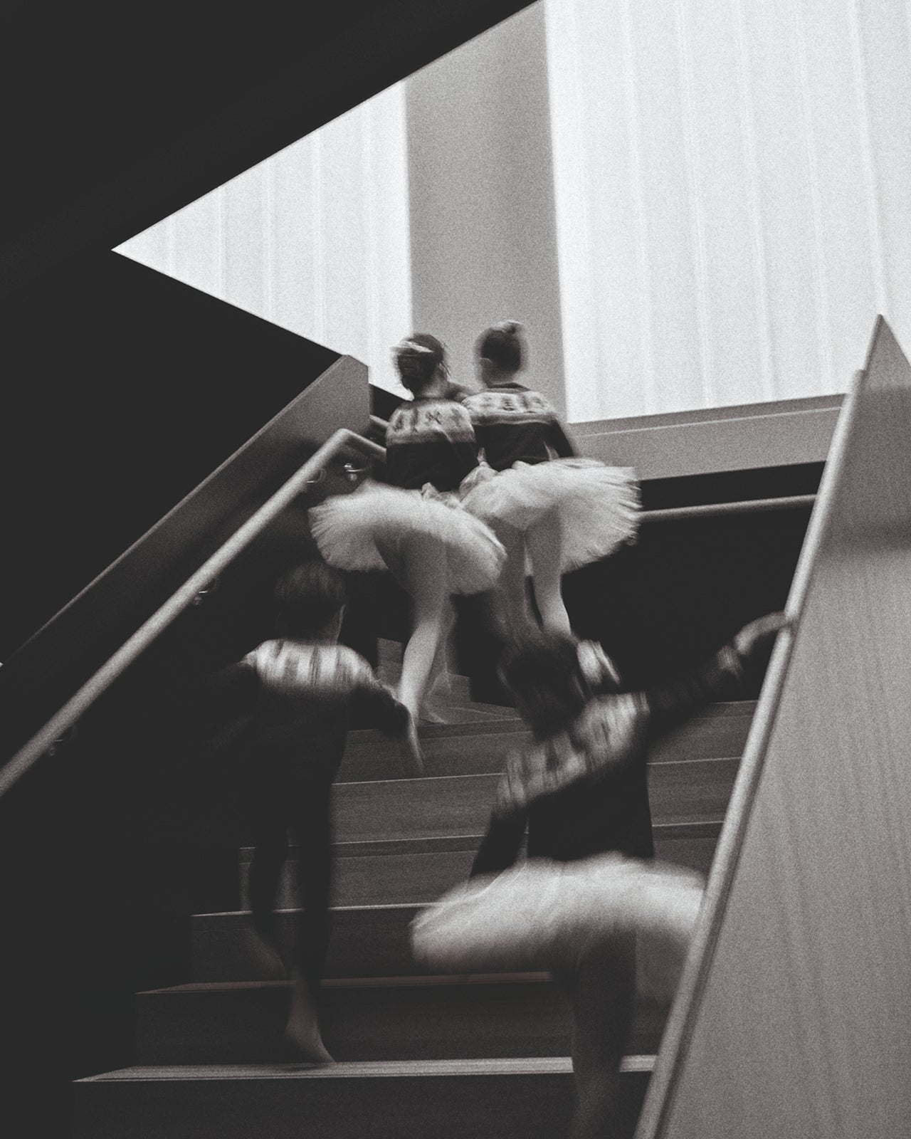 Two ballerinas in tutus walking up a staircase.