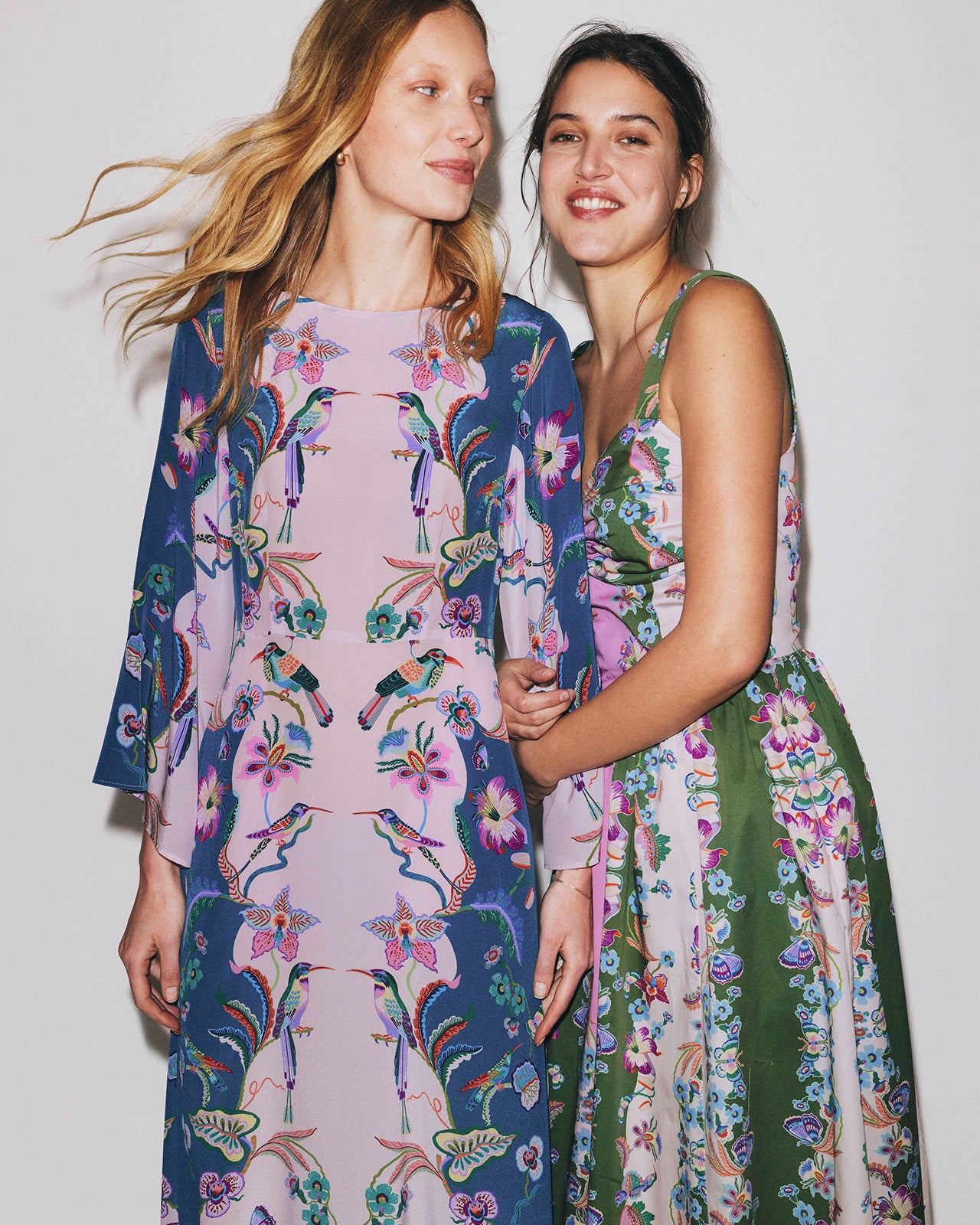 Two women wearing floral and bird-patterned dresses against a plain background