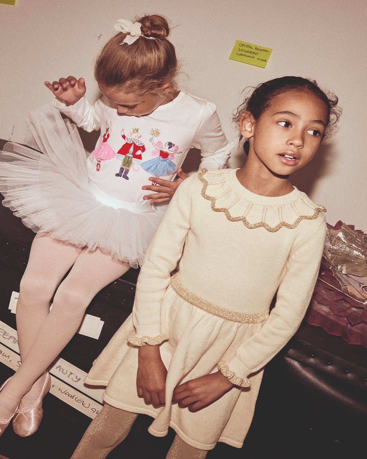 Two young girls in dresses standing next to each other indoors.
