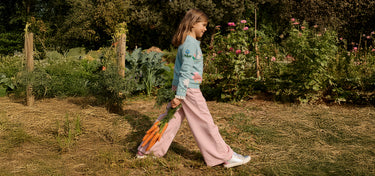 Person walking through a garden holding carrots with greenery and flowers in the background