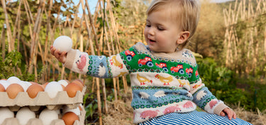 Child in a colorful sweater interacting with eggs outdoors