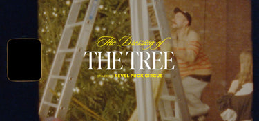 Two people on ladders near a Christmas tree with text overlay 'The Dressing of THE TREE' and 'Revel Puck Circus'.