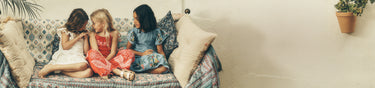 Three women sitting on a couch with decorative pillows and a plant in the background
