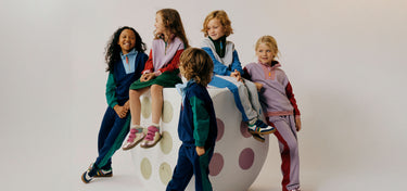 Five children in colorful outfits sitting on a polka dot chair against a white background