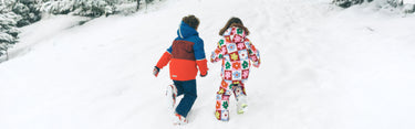 Two children in colorful winter outfits walking on a snow-covered path.