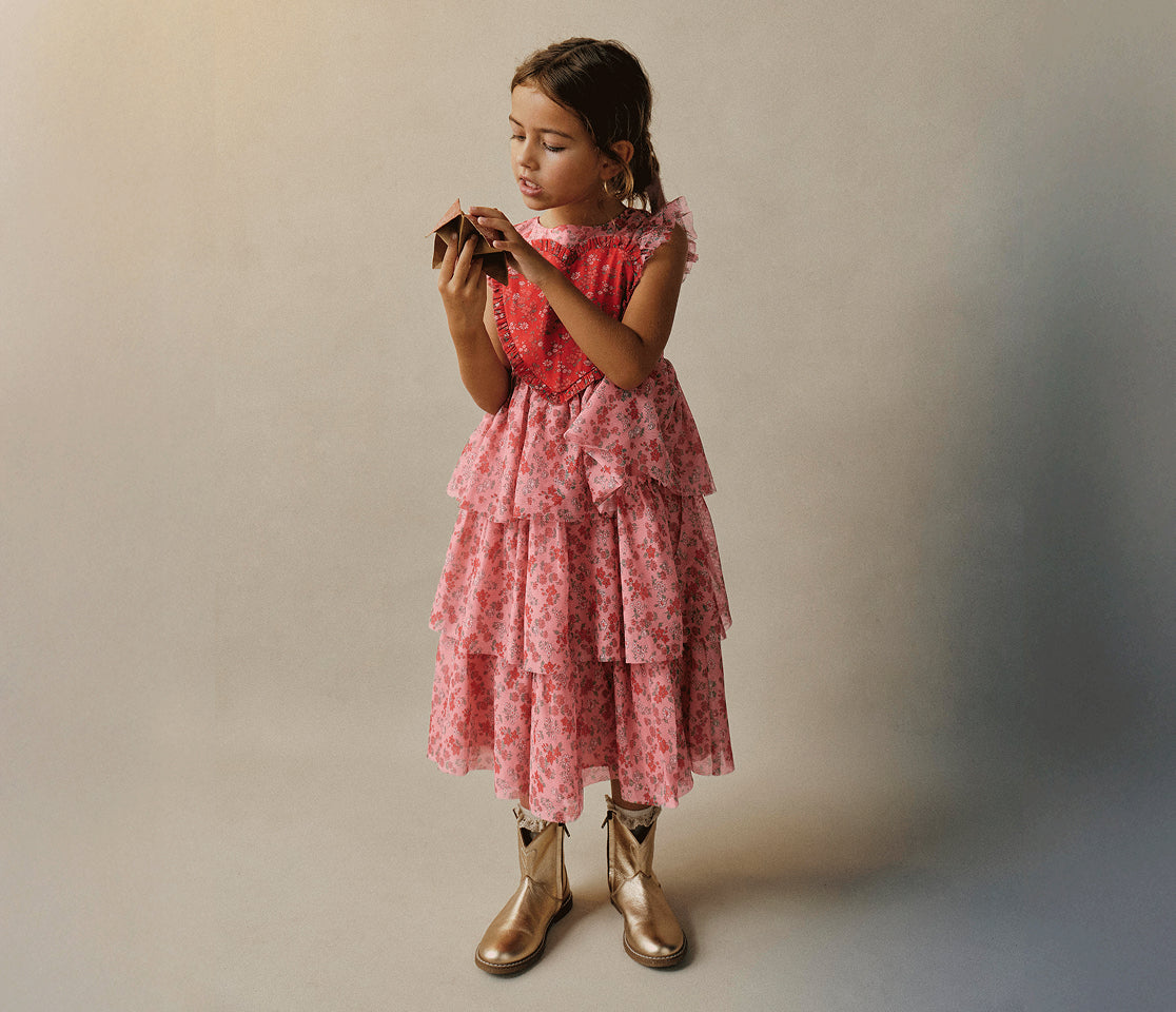 Young girl in a pink floral dress standing against a plain background