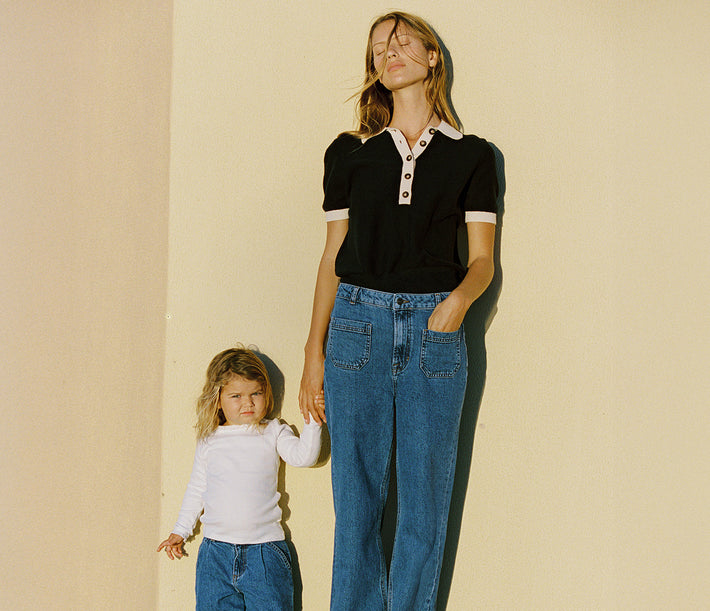 Woman and child standing against a beige wall, both wearing jeans.