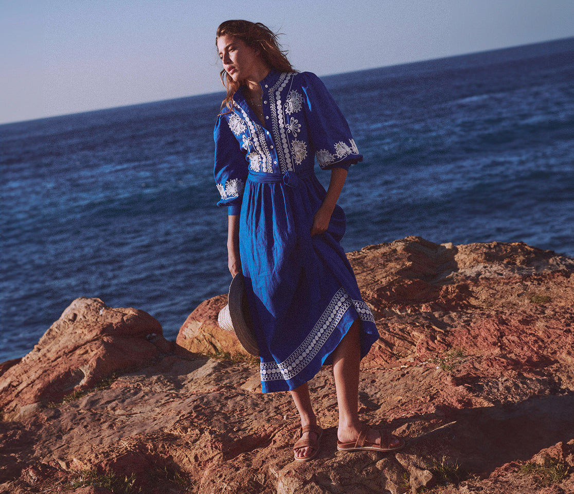 Woman in a blue dress standing on rocky terrain by the ocean